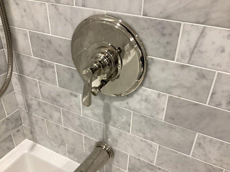 Conducted follow-up site visit to assess shower valve system requiring replacement parts. Inspected chrome shower fixture assembly mounted on marble-patterned tile surround, including pressure-balance valve control, handheld showerhead with flexible hose, and sliding bar system. Documented installation configuration and verified part specifications needed for ordering, with photos taken for reference to ensure correct component procurement for upcoming repair completion.