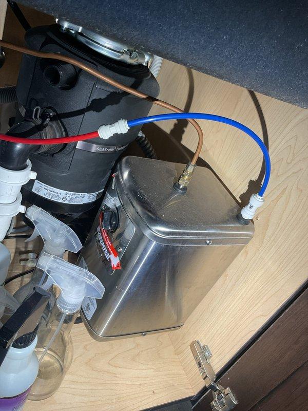 Responded to a leak at the connection point on an Everpure water filtration system installed in an under-cabinet location. Inspected the black cylindrical filter unit and associated plumbing connections, identifying the source of the leak at one of the top-mounted connection ports where white and gray supply lines interface with the filter housing. Tightened and resealed the compromised connection to eliminate the leak and restore proper system operation.