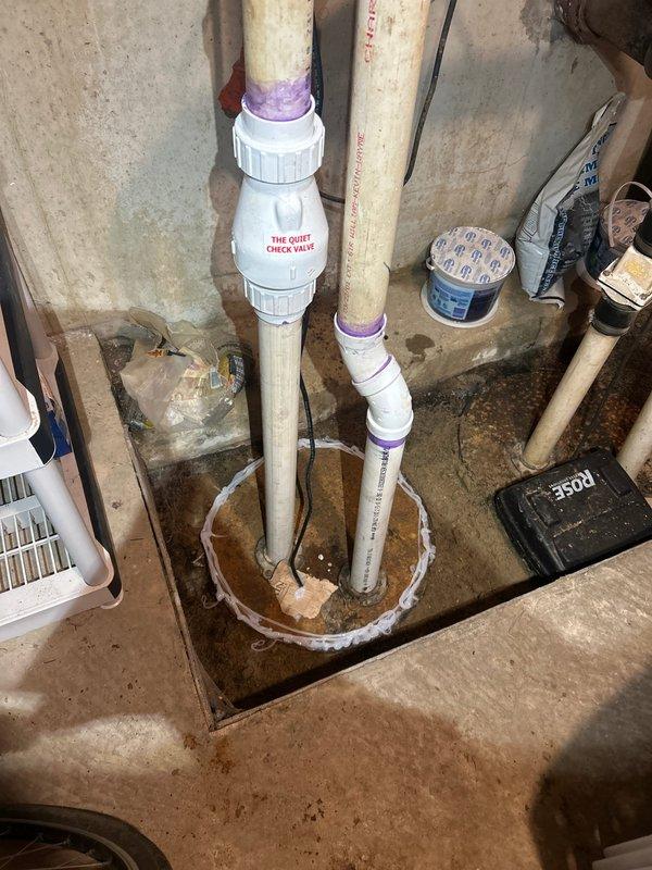Completed waste pump installation in basement utility area with new PVC discharge piping system. Installed vertical discharge lines with proper check valve integration, secured all pipe penetrations through concrete floor with appropriate sealing, and verified system operation. All components installed to code specifications with purple primer applied at joints for proper solvent welding of PVC connections.