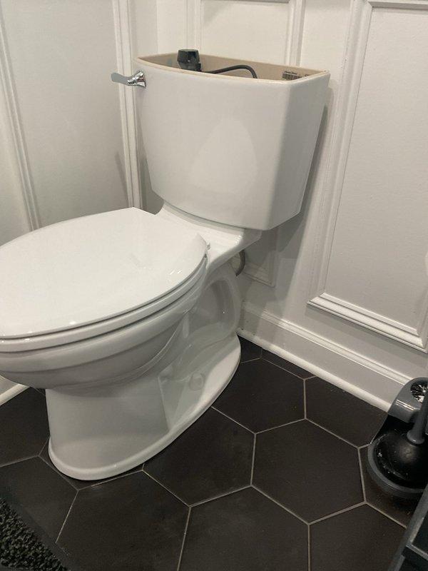 Completed toilet installation in residential bathroom featuring white two-piece porcelain fixture with chrome flush handle. Replaced existing unit that exhibited severe condensation and frost buildup behind tank area, indicating previous supply line or seal failure. New installation includes proper water supply connection, wax ring seal, and secure mounting to ensure leak-free operation and prevent moisture intrusion that caused the crystalline ice formation observed on the previous fixture.