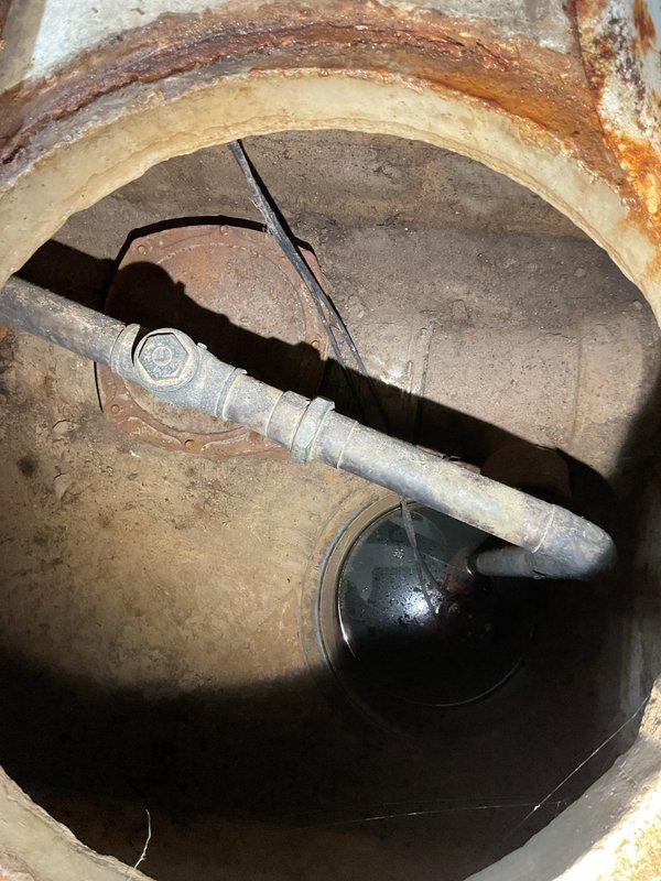 Responded to a flood control system failure caused by a broken check valve in the underground flood control pit. Upon inspection, found the check valve mechanism installed in 2020 had failed, compromising the system's ability to prevent backflow. The galvanized piping showed corrosion and the float mechanism at the base of the concrete pit required replacement. Documented extensive rust staining and deterioration throughout the concrete structure and surrounding floor area, indicating prolonged moisture exposure. Photographed the damaged check valve assembly, corroded piping connections, and the condition of the utility room floor with significant water damage patterns around the drain cover and equipment. Provided assessment and repair recommendations to restore proper flood control system functionality.