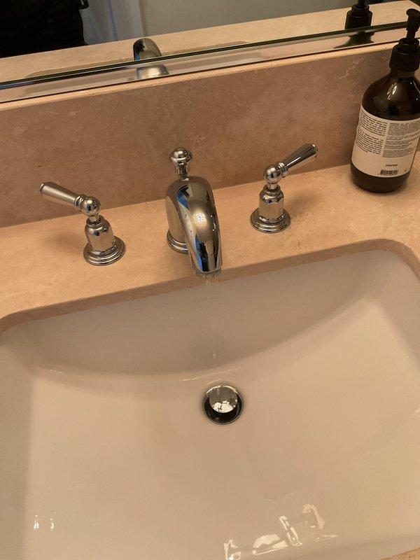 Responded to service call for multiple plumbing leaks including an exterior hose bib, bathroom faucet, and PVC pipe near furnace. Inspected weathered brass outdoor spigot mounted on brick exterior wall showing signs of deterioration and active leak. Evaluated bathroom sink with three-piece chrome faucet assembly featuring separate hot and cold handles and center spout, identifying source of leak at fixture. Documented conditions of both locations with photographs for repair assessment and provided recommendations for necessary repairs to resolve all reported leaking fixtures.