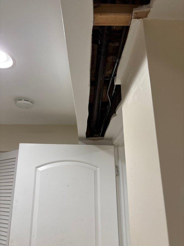 Accessed concealed plumbing system through ceiling cavity by creating rectangular access opening in drywall above entryway. Exposed and inspected dark water supply or drain lines running through ceiling joists and wooden framing members. Completed necessary repairs to piping system and left access opening in place for future maintenance requirements.