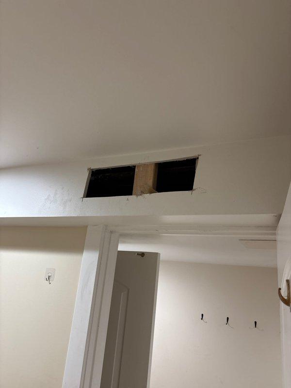 Accessed concealed plumbing system through ceiling cavity by creating rectangular access opening in drywall above entryway. Exposed and inspected dark water supply or drain lines running through ceiling joists and wooden framing members. Completed necessary repairs to piping system and left access opening in place for future maintenance requirements.