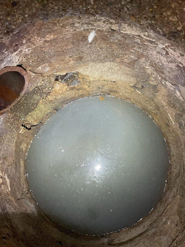 Responded to callback for underground sump pit or utility chamber inspection. Upon arrival, documented existing conditions showing significant sediment buildup, standing water accumulation, and deteriorated interior surfaces with heavy mineral deposits and staining throughout the cylindrical concrete chamber. Identified drainage pipe entry point with visible moisture infiltration patterns and confirmed water level at bottom of pit, indicating potential drainage or pumping system concerns requiring attention.