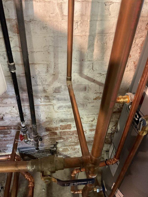 Responded to clogged drain service call and conducted comprehensive inspection of basement plumbing system. Upon arrival, assessed the drainage infrastructure including exposed copper supply lines, PVC drain piping, and floor drain assembly. Documented existing plumbing configuration with copper pipe runs, brass fittings, and drainage connections throughout the mechanical space. Inspected floor drain location and surrounding plumbing components to identify potential blockage points in the drainage system. Photographed the plumbing layout for service records, capturing vertical and horizontal pipe runs, shut-off valves, and connection points along the cinderblock foundation wall.