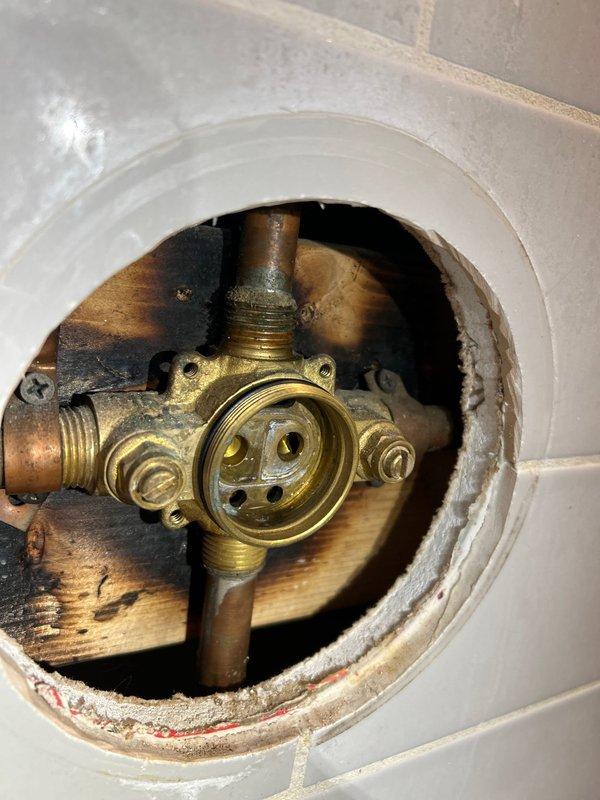 Responded to service call for shower cartridge replacement in tub/shower combination unit. Upon arrival, accessed plumbing valve assembly through existing wall access opening to assess cartridge compatibility. Customer had previously removed original faucet and handle, and provided replacement Glacier Bay shower handle and tub faucet components with uncertainty about proper fitment. Inspected brass valve body and threaded connections behind wall-mounted access panel to verify cartridge specifications and compatibility with customer-supplied fixtures. Evaluated existing plumbing configuration including shower arm, escutcheon plate, and valve assembly condition. Confirmed proper installation requirements and provided assessment of replacement parts compatibility with existing rough-in valve system.