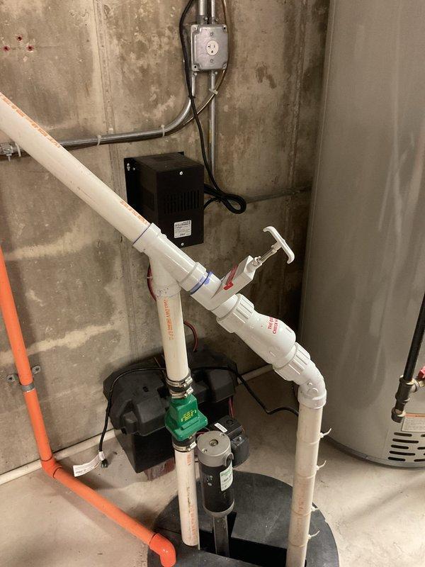 Completed installation of new sump pump system with battery backup in basement utility area. Installed primary sump pump in black basin with vertical PVC discharge piping, including check valve and control handle assembly, connected electrical components with wall-mounted control unit and junction box, and integrated battery backup system to ensure continuous operation during power outages.