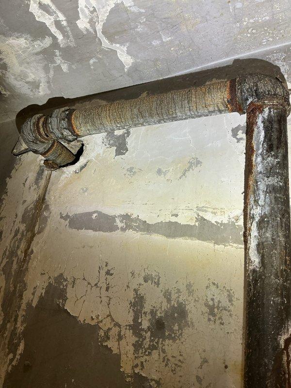Conducted comprehensive assessment of aging water service line and associated plumbing infrastructure displaying severe corrosion and deterioration. Documented existing conditions of galvanized steel piping system including vertical riser, horizontal supply lines, gate valve assembly, and threaded fittings showing extensive rust, scaling, and compromised metal integrity. Identified moisture staining on concrete flooring near pipe base and evaluated structural condition of corroded connections requiring replacement. Photographed deteriorated plumbing components to support estimate preparation for complete water service line upgrade and valve replacement.