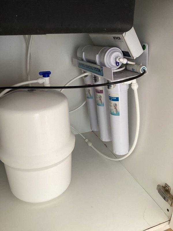 Responded to a priority service call for a leaking reverse osmosis water filtration system located under the kitchen sink. Upon inspection, identified the source of the leak within the multi-stage RO system, which consisted of vertically-mounted white cylindrical filter cartridges connected by white plastic tubing and a pressurized storage tank with blue valve fitting. Performed necessary repairs to eliminate the leak, verified all connections and fittings were secure, and tested the system for proper operation and water flow through all filtration stages.