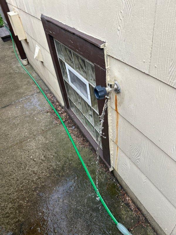 Installed new Prier quarter-turn outdoor water spigot on exterior wall near window, replacing old leaking fixture that had caused rust staining on the siding. The new frost-free valve features a 90-degree quarter-turn operation with green handle for easy shutoff and brass construction for durability.