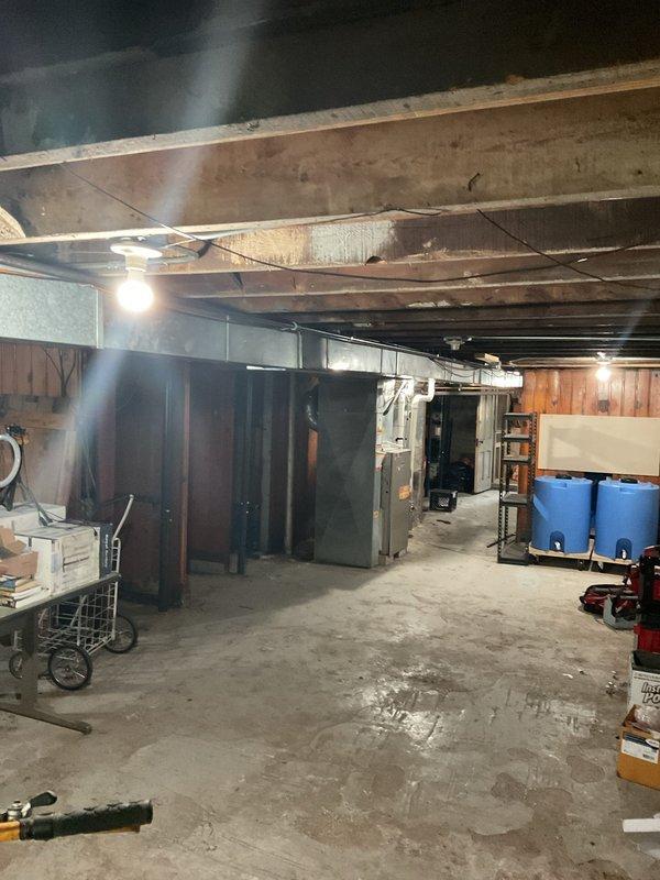 Completed plumbing piping installation in unfinished basement utility area. Installed new piping infrastructure throughout the space, working around existing structural elements including exposed ceiling joists, support posts, and concrete beams. Routed piping to accommodate stored equipment and maintain clearances for future access to utility systems.