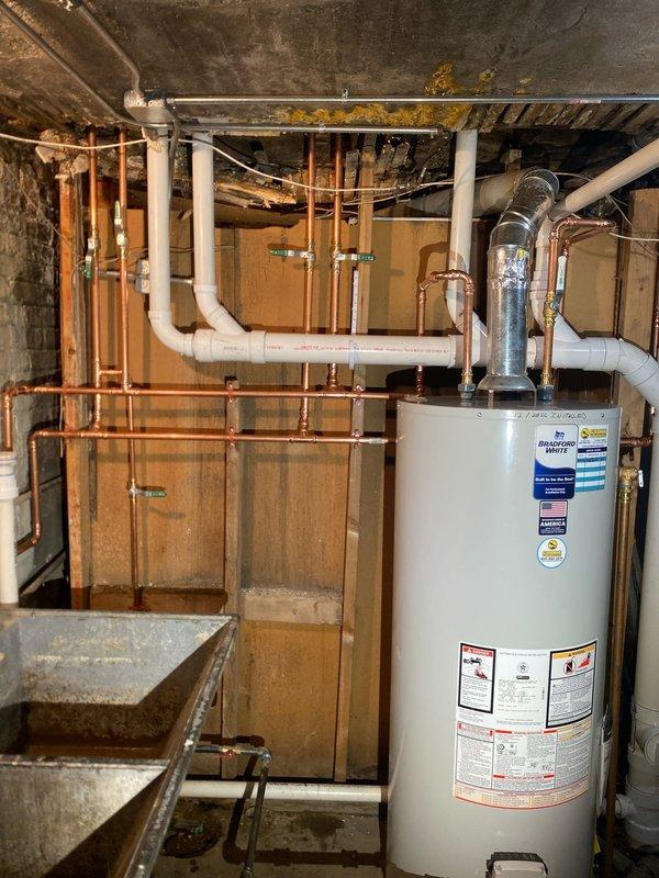 Conducted comprehensive assessment of residential basement plumbing and water heating system. Inspected existing white cylindrical water heater, associated copper supply lines, brass valves, flexible metallic venting, and PVC drainage connections for proper operation and code compliance. Evaluated galvanized utility sink, overhead copper piping network, and drainage system throughout unfinished basement mechanical room. Documented current conditions of all plumbing infrastructure, including aging copper lines with natural patina, PVC pipe routing, and water heater connections to facilitate scheduled repair work.