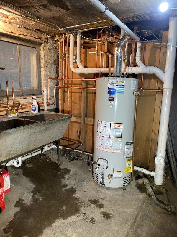 Conducted comprehensive assessment of residential basement plumbing and water heating system. Inspected existing white cylindrical water heater, associated copper supply lines, brass valves, flexible metallic venting, and PVC drainage connections for proper operation and code compliance. Evaluated galvanized utility sink, overhead copper piping network, and drainage system throughout unfinished basement mechanical room. Documented current conditions of all plumbing infrastructure, including aging copper lines with natural patina, PVC pipe routing, and water heater connections to facilitate scheduled repair work.