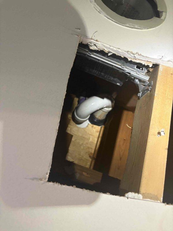Responded to commercial water leak in basement storage area where ceiling leak had been reported with drywall already removed for access. Performed leak location investigation through exposed ceiling cavity, identifying PVC plumbing line entering from above as the source area. Documented existing conditions including exposed framing, curved drain/vent piping, and access opening with structural supports visible. Completed photo documentation of leak source location and surrounding plumbing infrastructure for repair planning and further remediation work.
