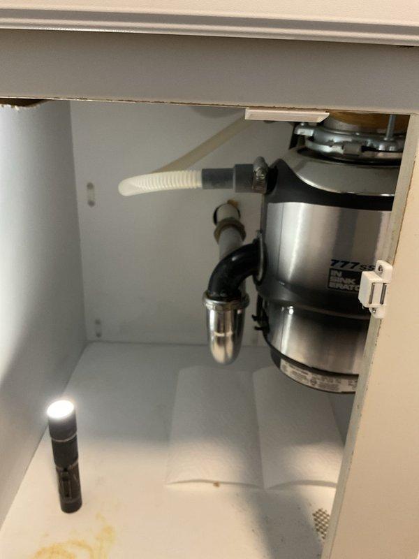 Responded to priority appointment for kitchen sink drainage issue. Upon inspection, identified failed P-trap assembly connected to garbage disposal unit requiring replacement. Removed deteriorated chrome P-trap and associated fittings from disposal outlet. Installed new P-trap assembly with proper connections to garbage disposal and drain line, ensuring secure threaded fittings and proper trap seal. Verified all connections for leaks and confirmed proper drainage flow through system. Documentation photos captured before and during repair showing cabinet interior, existing plumbing configuration, and disposal unit connections.