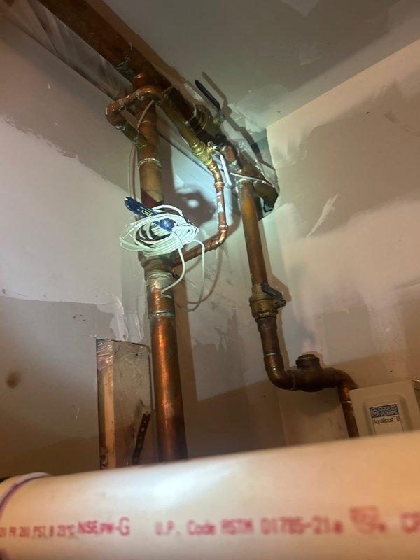 Responded to outdoor spigot leak caused by freeze damage from winter conditions. Inspected exterior hose bib mounted on concrete block wall and traced supply line to interior plumbing connections. Documented damaged frost-free spigot and associated copper supply piping that sustained freeze-related failure. Assessed interior plumbing configuration including copper pipe runs, brass fittings, and mounting hardware to determine extent of repairs needed for proper restoration of outdoor water supply system.
