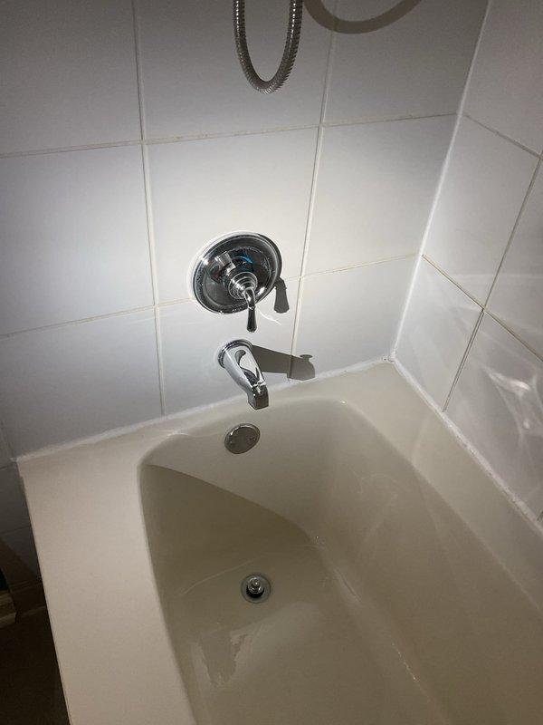 Responded to service call for dripping tub faucet in bathroom with white tiled walls and chrome fixtures. Inspected single-handle shower control with tub spout assembly and identified source of leak. Documented existing conditions of bathtub plumbing system including wall-mounted fixtures, spout, and drain assembly for repair recommendations.