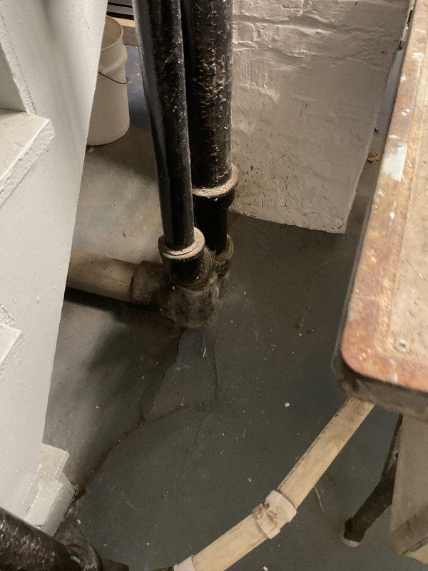 Performed camera inspection of basement drainage system to assess condition of aging cast iron plumbing infrastructure. Inspection revealed heavily corroded vertical drain pipes with significant mineral deposits, deterioration of pipe fittings, and standing water present on basement floor indicating potential drainage issues or backup in the system.