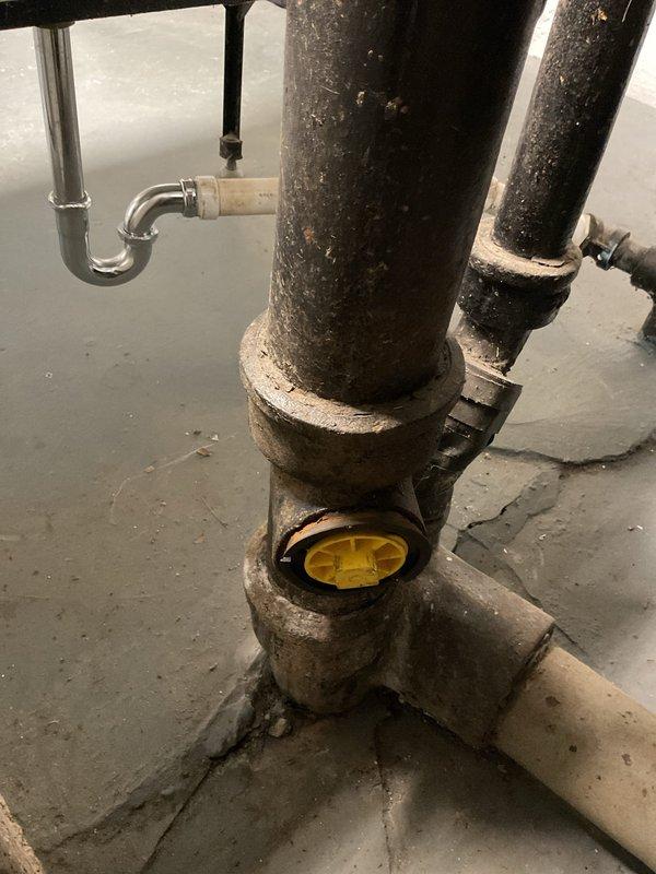 Performed camera inspection of basement drainage system to assess condition of aging cast iron plumbing infrastructure. Inspection revealed heavily corroded vertical drain pipes with significant mineral deposits, deterioration of pipe fittings, and standing water present on basement floor indicating potential drainage issues or backup in the system.