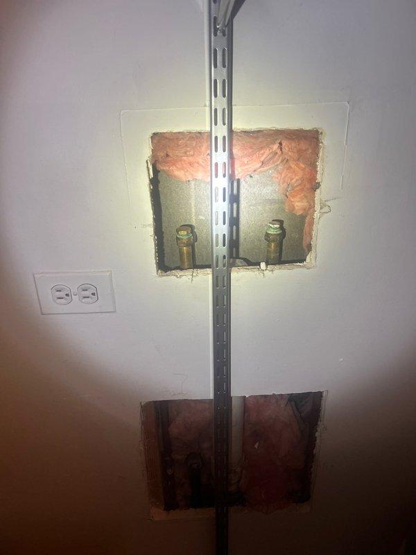 Activated washer/dryer hookups on second floor by uncapping existing gas line and installing shut-off valves for new appliances. Accessed plumbing infrastructure through wall openings, installed brass valves on gas supply lines, and secured connections with perforated metal mounting strut for proper support. Connections had been capped since original construction 25 years ago and were successfully restored to operational status for immediate appliance installation.