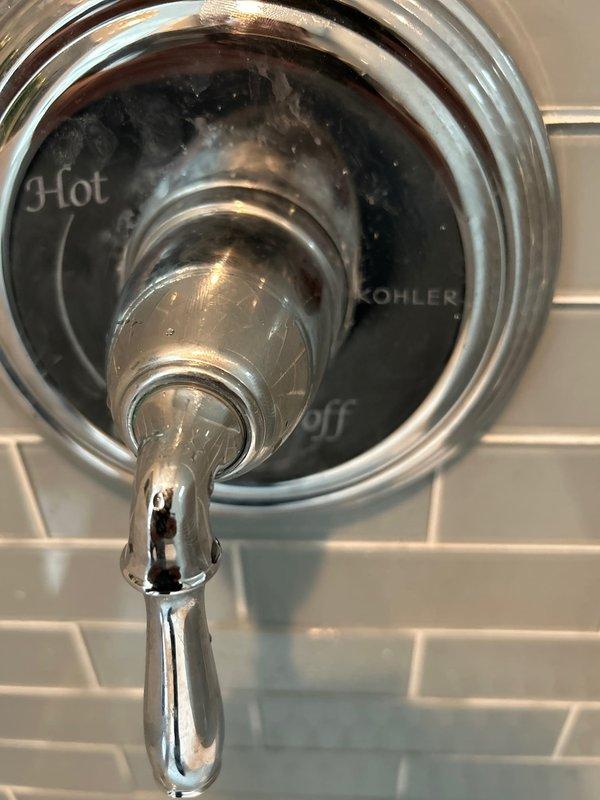 Replaced defective Kohler shower cartridge and installed new chrome trim plate on tiled shower wall. Accessed valve assembly through wall opening, removed old cartridge with brass-threaded connections, and installed replacement unit. Secured new trim plate with proper alignment, ensuring hot/cold markings were correctly positioned, and verified proper operation of single-handle shower control system.
