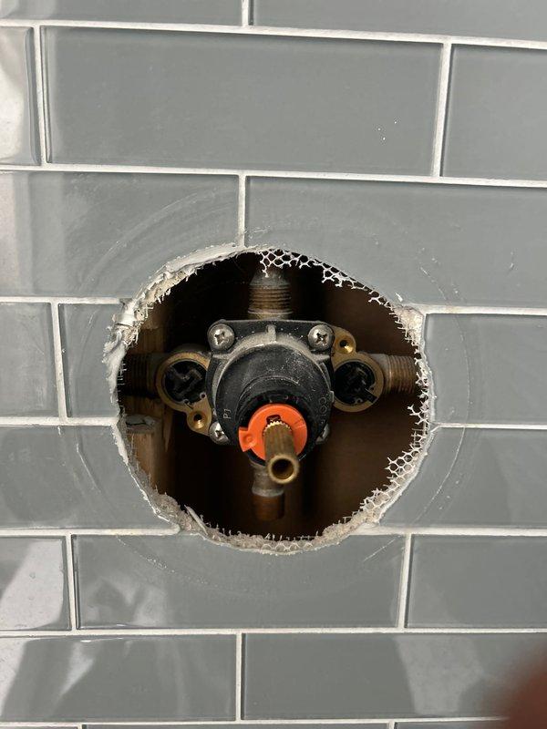 Replaced defective Kohler shower cartridge and installed new chrome trim plate on tiled shower wall. Accessed valve assembly through wall opening, removed old cartridge with brass-threaded connections, and installed replacement unit. Secured new trim plate with proper alignment, ensuring hot/cold markings were correctly positioned, and verified proper operation of single-handle shower control system.