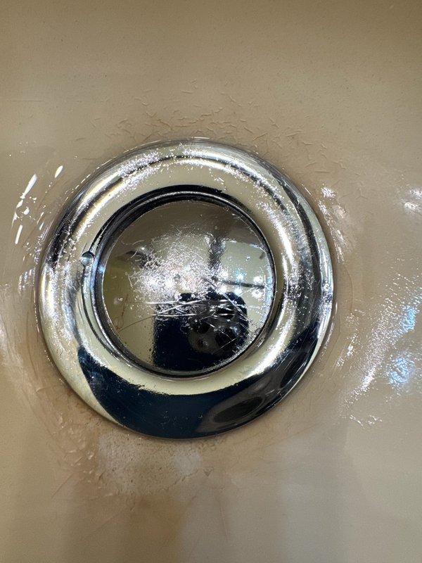 Responded to service call for stuck bathroom sink stopper. Successfully removed the malfunctioning pop-up drain assembly, which showed signs of mineral buildup and water spotting that had caused the stopper mechanism to seize. Disassembled the drain tailpiece and cleaned all components. Documented existing conditions with photographs showing the chrome drain fixture in the sink basin and the removed tailpiece assembly. Customer presented with repair estimate for consideration.
