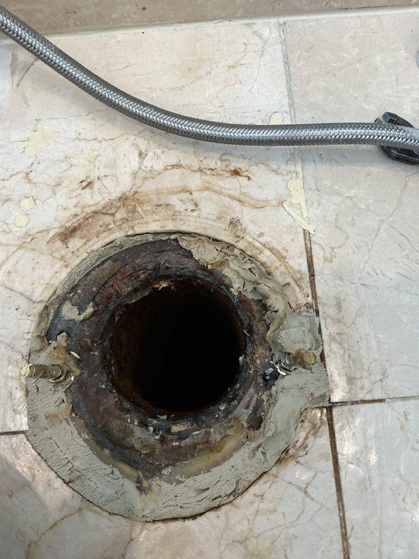 Responded to service call for toilet leaking at base, which was originally installed by our company one year prior and potentially under warranty. Upon inspection, discovered deterioration and corrosion around the toilet flange area with visible water damage and staining on the surrounding floor tiles. Documented existing conditions including rusted flange collar and compromised wax ring seal. Assessed the flexible braided water supply line connection and verified proper installation. Provided customer with diagnostic findings and repair recommendations to address the leak at the toilet base.