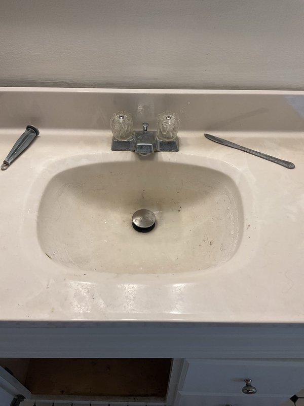 Responded to a second-floor bathroom sink drain stoppage that had persisted for several days in a century-old home. Upon arrival, inspected the white oval basin sink with chrome two-handle faucet and pop-up drain assembly. Accessed the cabinet beneath the vanity to examine the drainage system, which consisted of a black plastic tailpiece, white PVC P-trap assembly, chrome shut-off valve, and flexible supply line. Cleared the obstruction from the drain line, restoring proper water flow and drainage function. Tested the system to confirm complete resolution of the blockage and verified all plumbing connections remained secure with no leaks present.