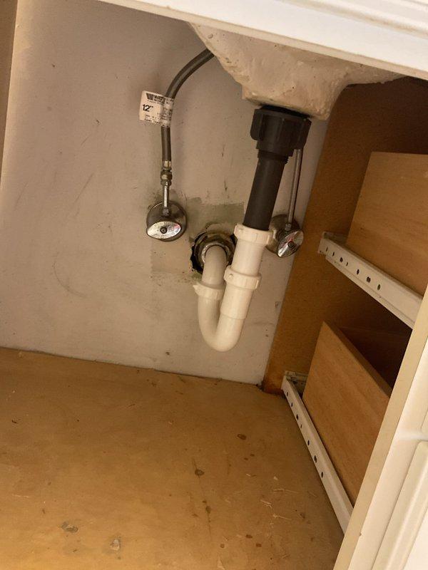 Responded to a second-floor bathroom sink drain stoppage that had persisted for several days in a century-old home. Upon arrival, inspected the white oval basin sink with chrome two-handle faucet and pop-up drain assembly. Accessed the cabinet beneath the vanity to examine the drainage system, which consisted of a black plastic tailpiece, white PVC P-trap assembly, chrome shut-off valve, and flexible supply line. Cleared the obstruction from the drain line, restoring proper water flow and drainage function. Tested the system to confirm complete resolution of the blockage and verified all plumbing connections remained secure with no leaks present.
