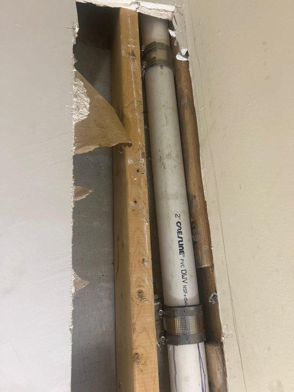 Responded to active water leak caused by accidental drilling through main 2" PVC DWV pipe during picture hanging attempt. Accessed damaged pipe through wall opening near laundry area, assessed extent of penetration damage to drainage system, and documented existing plumbing configuration including adjacent copper supply lines. Provided estimate for pipe repair including cutting out damaged section, installing new PVC coupling and pipe segment, pressure testing, and drywall restoration.