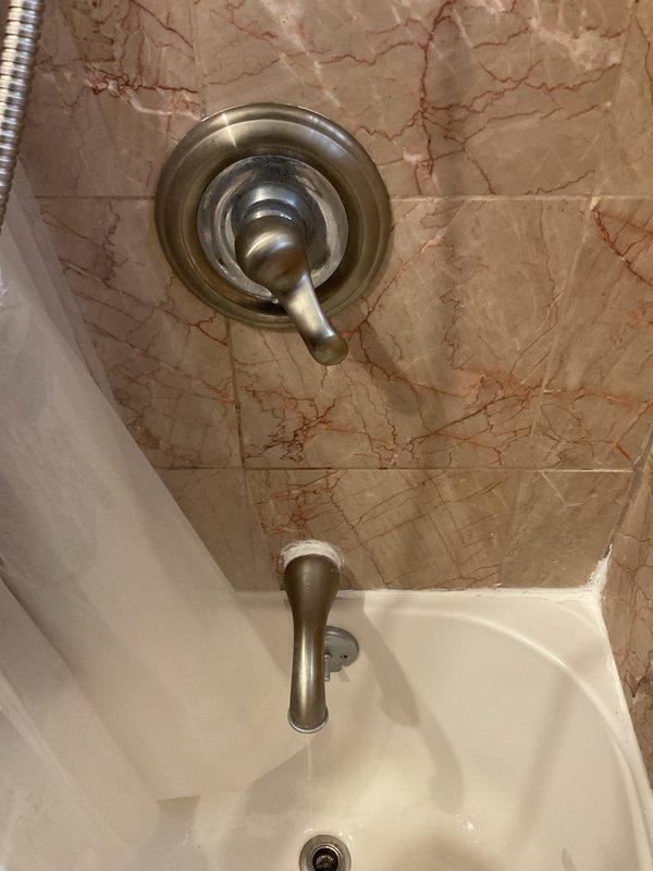 Responded to service call for malfunctioning push-type tub spout diverter that was failing to redirect water flow from tub spout to shower head. Inspected bathroom fixture assembly with brushed nickel finish mounted on marble tile surround and assessed diverter mechanism for failure points. Evaluated existing plumbing infrastructure in crawl space beneath fixture, documenting water supply lines with NIBCO valves and overall system condition to determine repair versus replacement requirements for the shower/tub valve system.