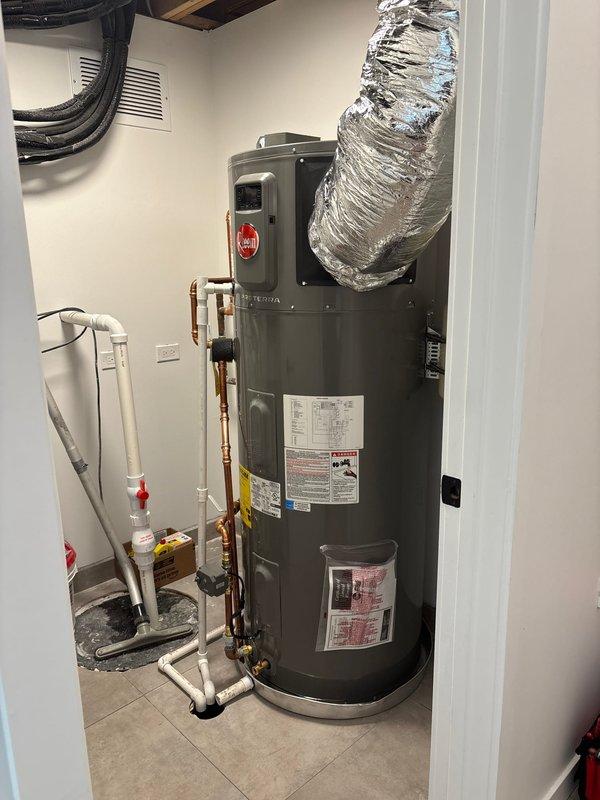 Completed follow-up call to schedule water heater replacement installation for Thursday. Customer's existing unit was previously diagnosed as faulty by manufacturer and is ready for replacement now that account balance has been cleared. Documented current equipment conditions with photos showing outdoor tankless unit with protective covering and indoor conventional water heater with existing plumbing connections, venting, and PVC drain lines in preparation for upcoming installation work.
