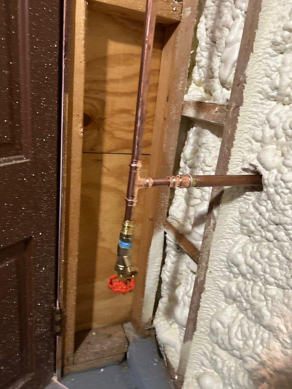 Responded to emergency call for split outdoor spigot supply line causing basement flooding. Located the failed copper pipe section within the wall cavity between studs, removed the damaged portion, and installed new copper piping with proper soldered joints and a brass shutoff valve with compression fittings. Applied spray foam insulation around the repaired plumbing to prevent future freeze damage, verified the exterior spigot connection was secure, and tested the system for leaks before restoring water service.