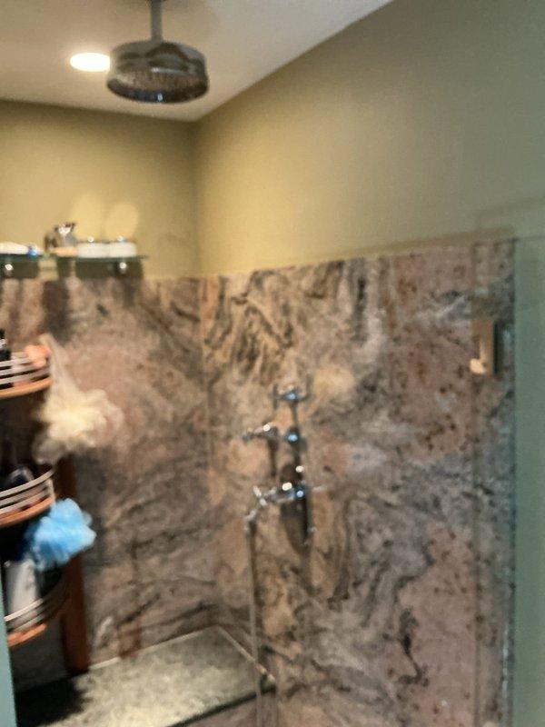 Completed installation of new chrome shower valve system in walk-in shower with polished granite wall panels. Installed three-piece fixture assembly including upper and middle cross-handle valve controls and lower main control unit with diverter valve and circular escutcheon plate, along with handheld shower head attachment. All fixtures tested and verified for proper water flow, temperature control, and diverter operation with no leaks detected.