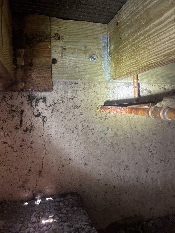 Inspected crawl space plumbing penetration through foundation wall where copper pipe enters structure. Documented existing foundation cracks and deterioration around pipe entry point. Assessed structural framing, floor joists, and support systems in crawl space area for potential water damage or concerns related to plumbing infrastructure. Photographed current conditions of pipe insulation, foundation wall integrity, and moisture indicators at grade level for customer records and future reference.