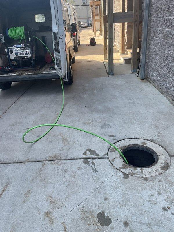 Responded to priority service call for hydrojetting at active construction site. Successfully deployed hydrojetting equipment to access underground drainage system through cleanout opening in concrete slab. Completed high-pressure water jetting procedure to clear drainage lines, with equipment and hoses positioned from service vehicle to reach underground access points in the construction area.