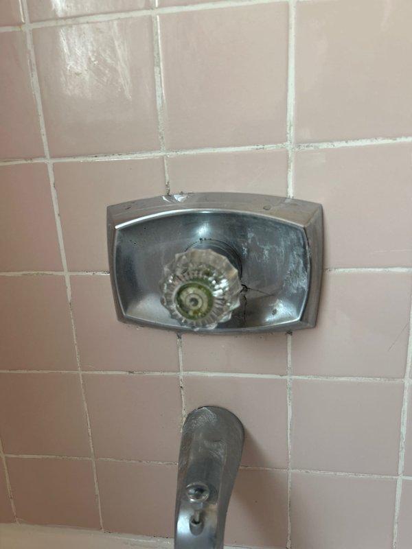 Responded to multiple plumbing concerns in a residential property including a toilet leaking at the base during flushing, potentially contributing to downstairs water damage, a shower temperature control valve malfunction preventing hot water delivery, and a deteriorated main water shut-off valve requiring replacement. Inspected vintage bathroom fixtures with pink tile surround, documenting the existing shower valve assembly with transparent faceplate and chrome tub spout showing age-related wear and mineral deposits. Assessed the toilet wax ring failure causing water seepage at the base and evaluated the corroded main shut-off valve that posed risk during operation.