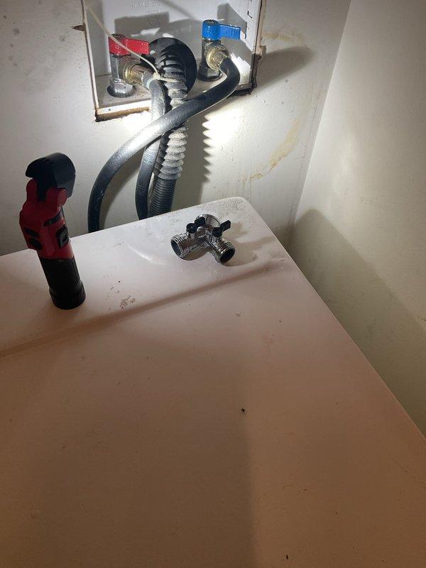 Conducted commercial drain and sewer estimate involving inspection of under-sink plumbing assembly with wall access panel. Assessment included evaluation of flexible supply lines, corrugated drainage tubing, shut-off valves with blue handles, and brass fittings for potential replacement or repair needs. Documented existing water staining on wall surfaces and multi-port valve connections requiring attention.