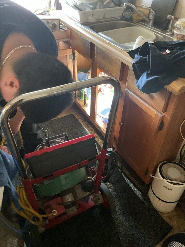 # Clogged Kitchen Sink Drain - Third Floor

Responded to a clogged kitchen sink drain line on the third floor. Deployed a 100-foot power rodding machine to mechanically clear the blockage in the kitchen sink drain line. Accessed the drain system through the cabinet beneath the sink and fed the rodding cable through the line to break up and remove the obstruction.

The power rodding equipment was positioned on protective matting in front of the sink cabinet to prevent floor damage during operation. The rodding process involved feeding the flexible cable with cutting head through the drain line to physically break apart accumulated debris and restore drainage flow.

Upon completion of the rodding service, tested the drain line for proper flow. Customer was advised that rodding service carries no warranty due to the nature of the work and potential for recurring blockages depending on underlying drain line conditions or usage patterns. Customer was informed that if full flow could not be 
