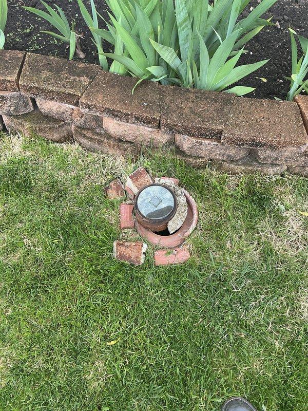 Completed cleanout repair on main sewer line access point, addressing damaged brick surround and performing rodding service to clear downspout drainage system. Repaired ground-level cleanout assembly with oxidized brass cap and restored functionality to the cylindrical pipe access point. Documentation photos captured pre-existing conditions including deteriorated brickwork around the cleanout and interior pipe condition showing rust discoloration and mineral deposits.