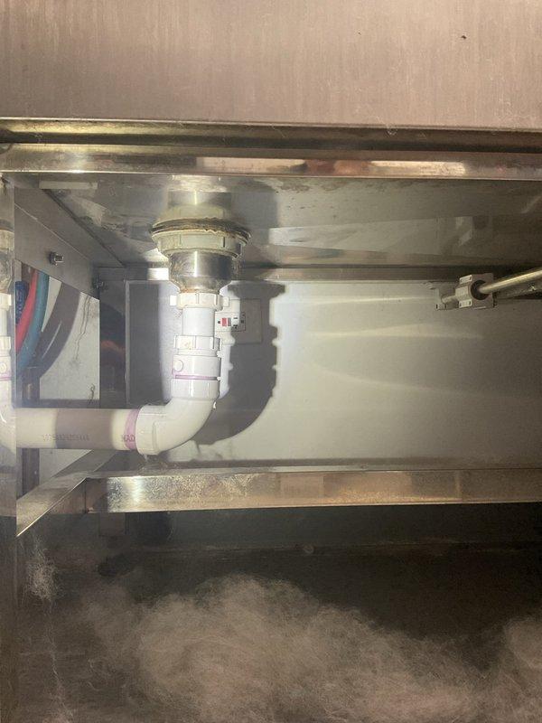 Completed commercial fixture installation for stainless steel sink with new drain assembly. Installed white PVC P-trap configuration with basket strainer and proper waste line connections, ensuring all plumbing components were secure and leak-free. Verified proper drainage function and left workspace clean with all connections tested and operational.