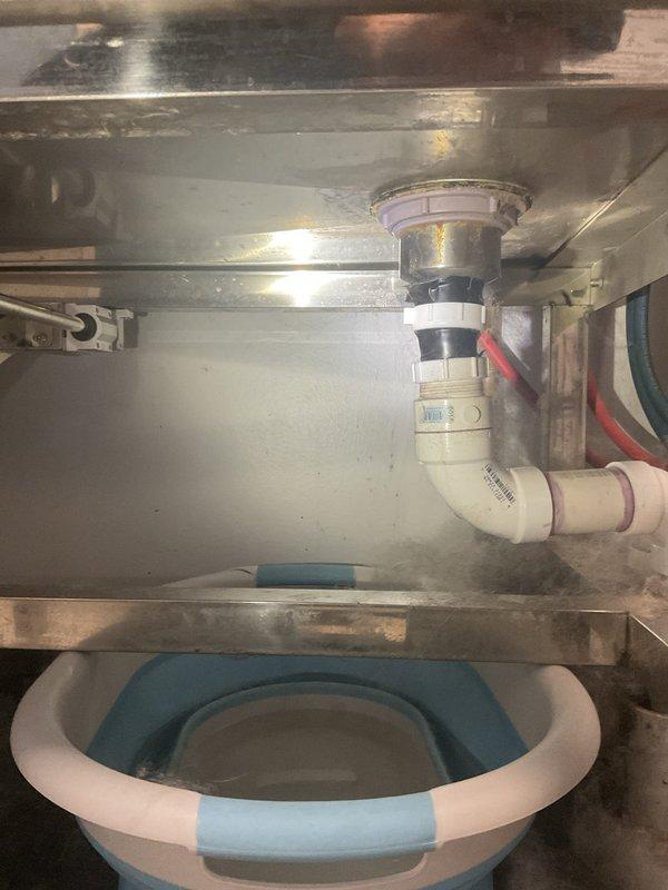 Completed commercial fixture installation for stainless steel sink with new drain assembly. Installed white PVC P-trap configuration with basket strainer and proper waste line connections, ensuring all plumbing components were secure and leak-free. Verified proper drainage function and left workspace clean with all connections tested and operational.