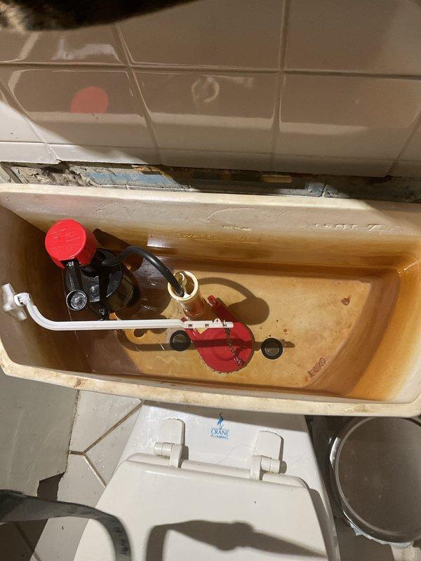 Responded to service call for toilet leaking onto bathroom floor. Upon inspection, removed tank lid and identified significant mineral deposits, rust buildup, and discolored water throughout the tank interior, indicating deteriorated internal components. The fill valve assembly and flush valve mechanism showed signs of age-related wear, with visible orange-brown staining on all ceramic surfaces and contaminated tank water. Documented existing conditions with photographs showing corroded internal mechanisms, including compromised rubber components and mineral accumulation affecting proper seal function. Diagnosed leaking issue as likely caused by failed flapper valve or deteriorated tank-to-bowl gasket allowing water to escape onto the floor. Presented repair options to address the active leak and restore proper toilet operation.