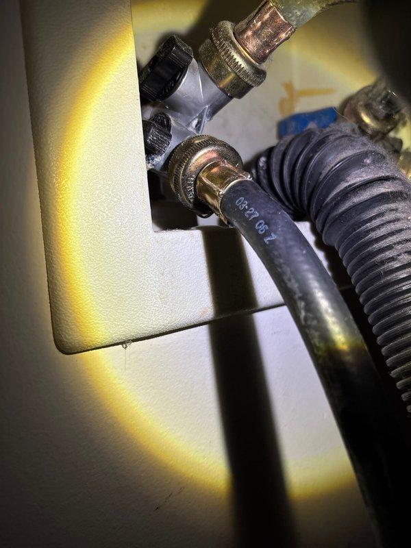 Responded to service call for leaking washing machine water line connector. Upon inspection, identified failed connection at the washer supply line fitting with visible water seepage. Accessed the plumbing assembly through existing wall panel, exposing copper supply lines, flex hoses, and shut-off valve. Replaced the defective threaded connector and brass fitting at the water supply line. Secured all connections with appropriate clamps and verified proper seal integrity. Tested the repair under full water pressure to confirm leak elimination and proper flow to the appliance.