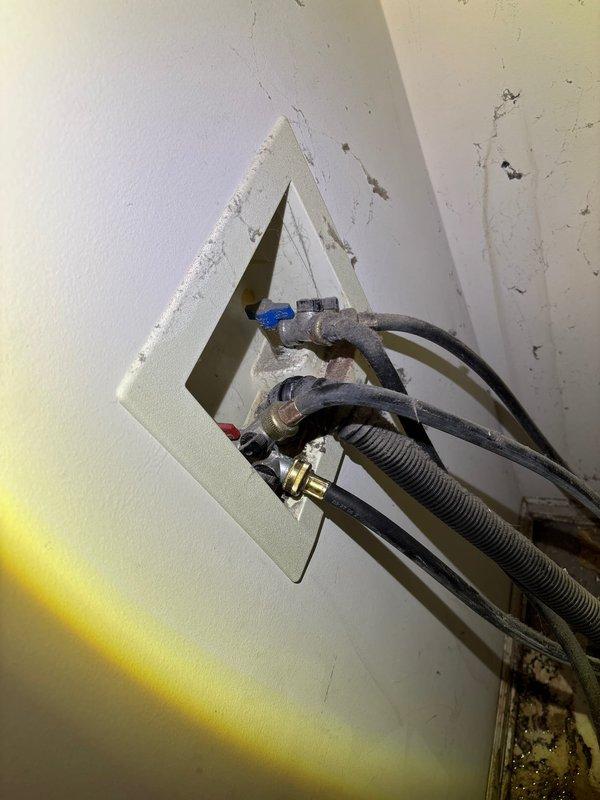 Responded to service call for leaking washing machine water line connector. Upon inspection, identified failed connection at the washer supply line fitting with visible water seepage. Accessed the plumbing assembly through existing wall panel, exposing copper supply lines, flex hoses, and shut-off valve. Replaced the defective threaded connector and brass fitting at the water supply line. Secured all connections with appropriate clamps and verified proper seal integrity. Tested the repair under full water pressure to confirm leak elimination and proper flow to the appliance.
