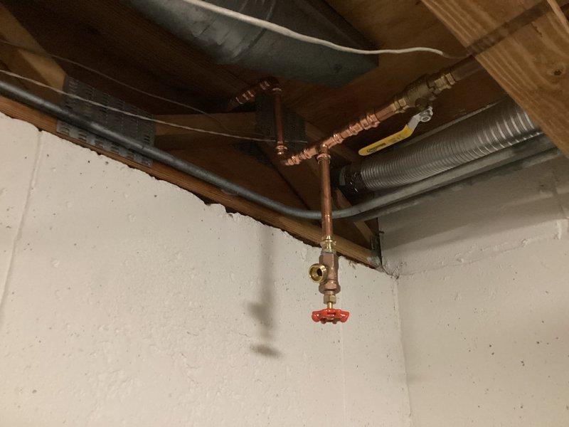 Responded to emergency repair call for burst copper pipe in basement utility area. Located the compromised section of copper piping along exposed ceiling joists near the wall junction. Shut off water supply using existing brass shutoff valve with red wheel handle to isolate the affected line. Removed damaged section of copper pipe and installed new copper piping with brass compression fittings, creating a proper T-junction configuration. Secured all horizontal runs with copper pipe straps to wooden joists per code requirements. Tested all connections for leaks, restored water supply, and verified system integrity. Documented existing plumbing configuration including HVAC ductwork and insulated lines in the overhead space for future reference.