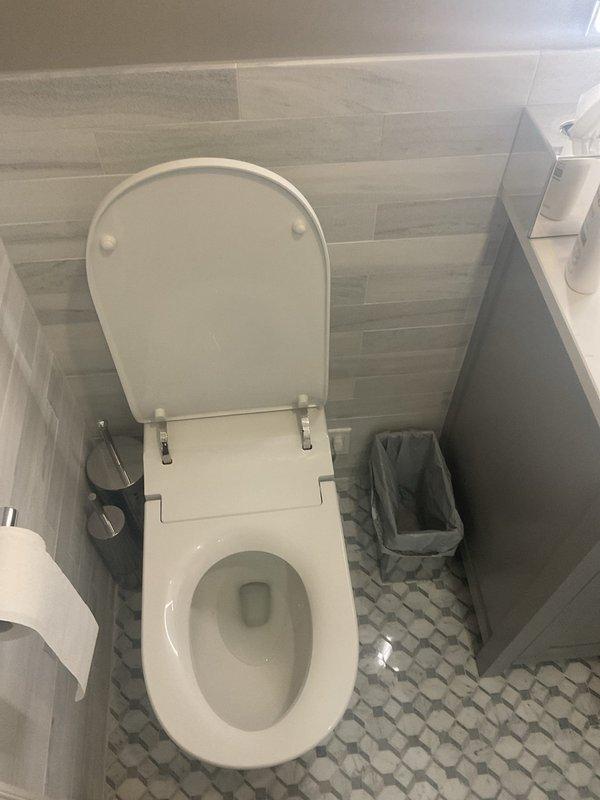 Responded to request for estimate to reposition toilet approximately 2 inches to center it properly in bathroom. Assessed existing toilet installation, floor tile configuration, and plumbing rough-in location to determine feasibility of relocation. Documented current toilet placement and surrounding bathroom layout including pebble-pattern floor tile and wall-mounted fixtures for estimate preparation.