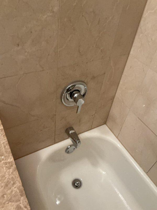 Responded to service call for recurring bathtub faucet drip and ceiling moisture concerns. Inspected chrome shower valve assembly and tub spout in tiled alcove bathtub installation. Assessed two areas of ceiling with visible water staining to identify potential leak sources above bathroom fixtures. Brought ladder for overhead access and replacement faucet components as requested due to ongoing issue requiring third visit.